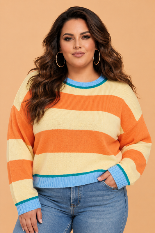 A woman wearing a Pretty Bash long-sleeve knit sweater with horizontal stripes in orange, cream, and light blue, paired with blue jeans, against a solid peach background.